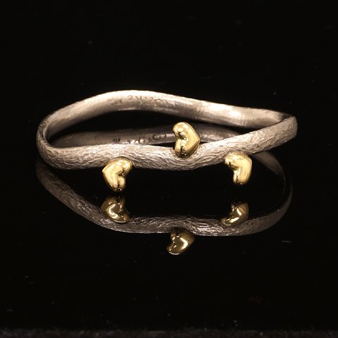 Michale Weihe: Oval armring i sterlingsølv med tre 
hjerter udført i 18kt guld. Indv. mål: 5,5x6,4cm. 
B: 0,6cm. V: 32gr